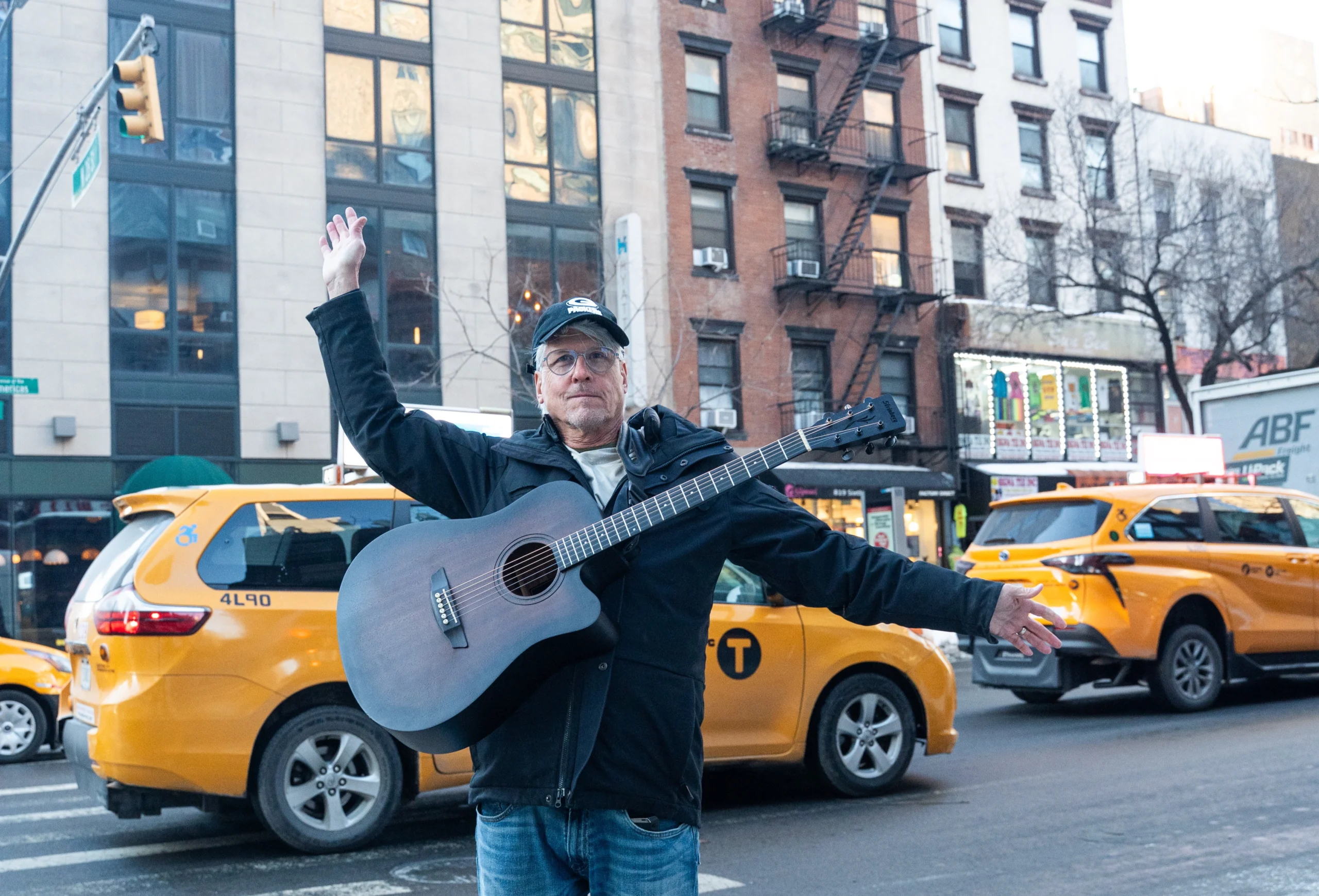 Man with guitar posting in front of NYC taxis