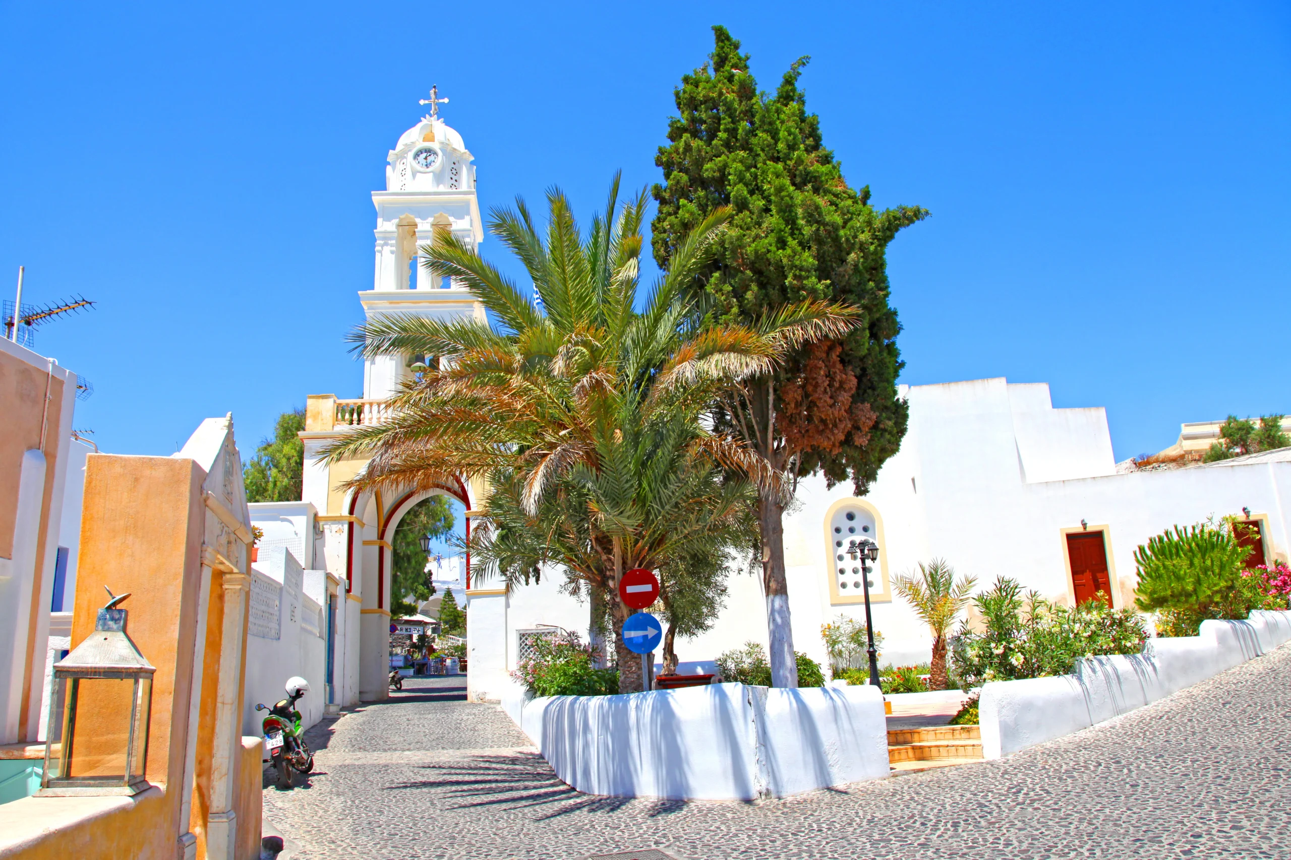 A narrow cobblestone street with an arched bell tower in the traditional village of Megalochori in Santorini