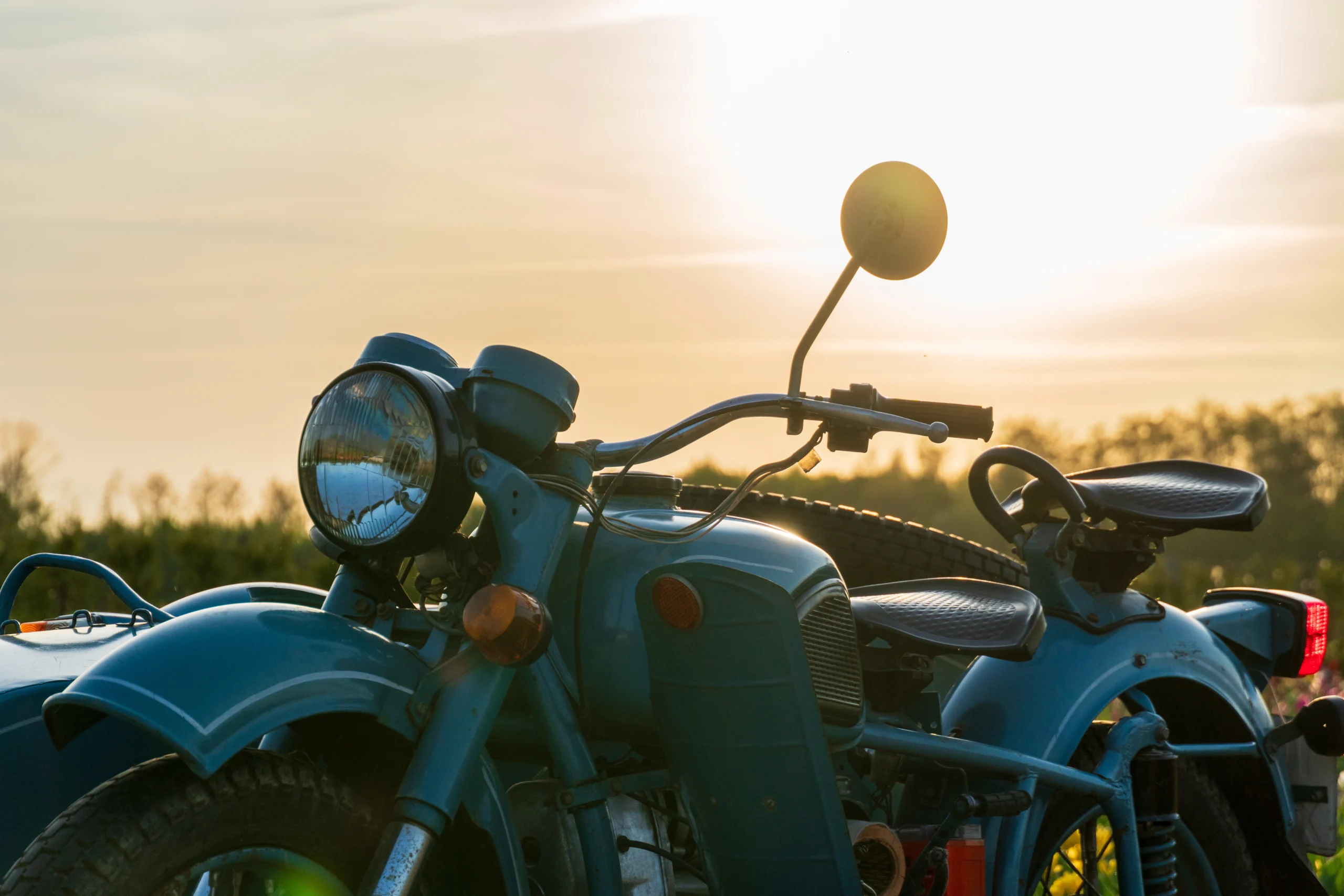 Vintage teal motorcycle with sidecar detail against warm sunset sky