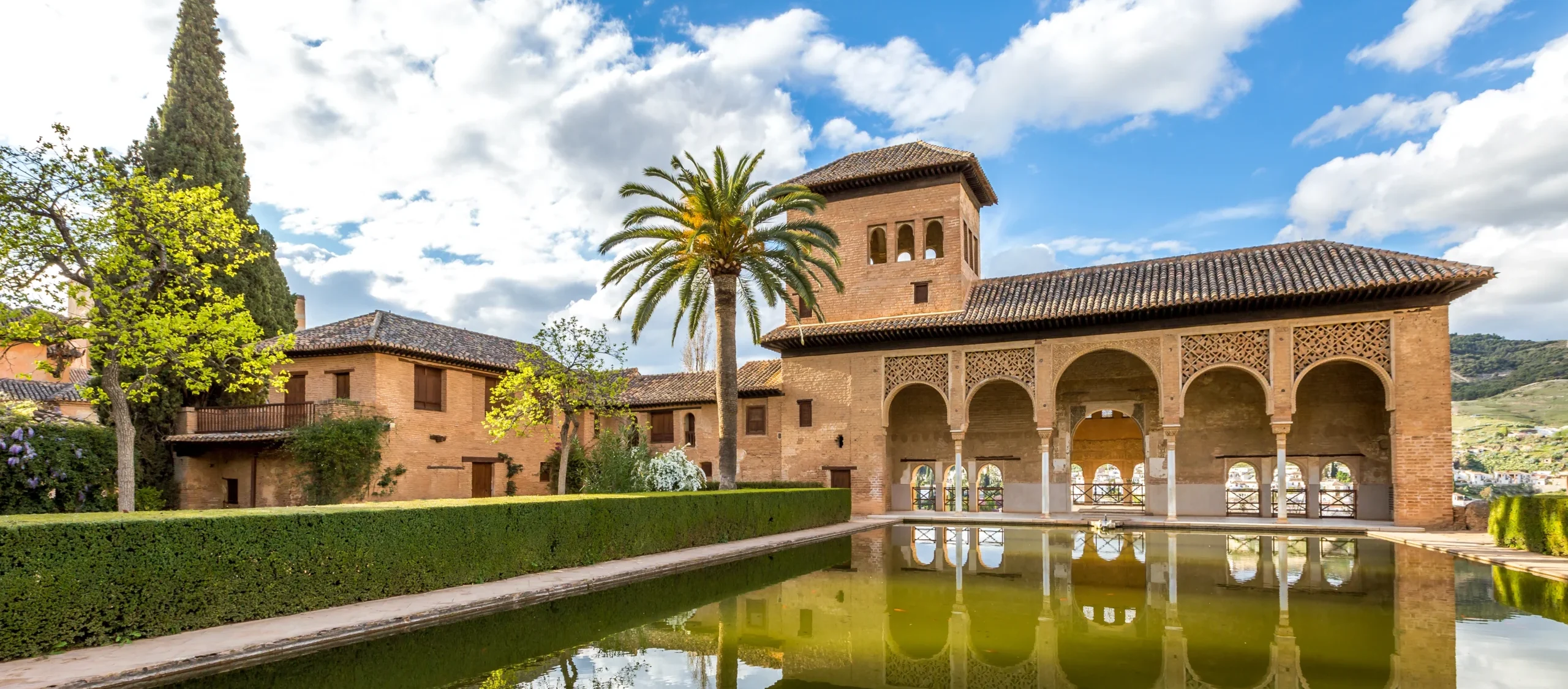 A large central pond faces the arched portico behind which stands the Tower of the Ladies, inside the Alhambra of Granada